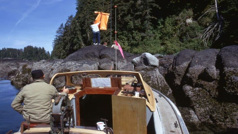 A boat near rocky terrain with people placing a bright orange flag on the rocks.