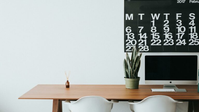 A sleek office desk with a computer, plant, and wall calendar