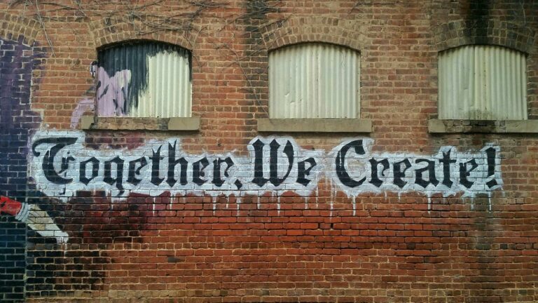 Brick wall with graffiti text 'Together We Create' painted in bold black letters.