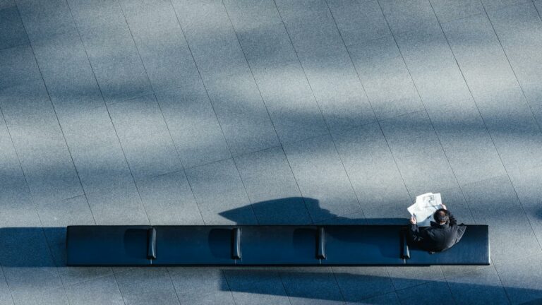 Person reading a newspaper on a bench in a large open space