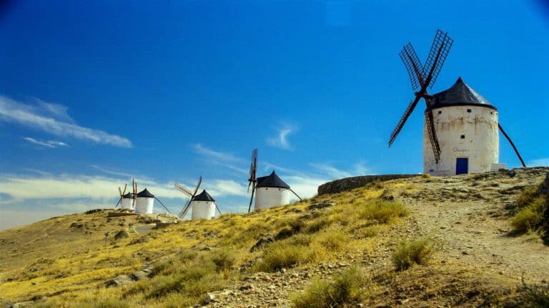 Traditional white windmills on a hilltop against bright blue sky in Consuegra, Spain