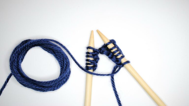 Mobile-optimized instructional image showing blue yarn cast onto wooden knitting needles for beginner knitting tutorial