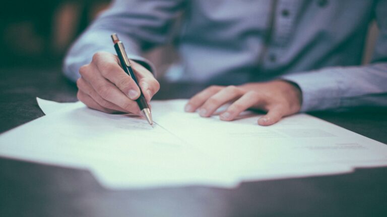 Person writing on documents at a desk, showcasing a website user interface concept