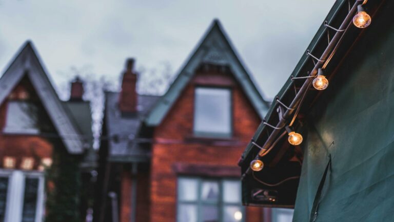 Victorian brick houses with gabled roofs and string lights hanging from eaves at dusk