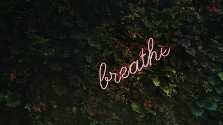 Neon sign reading 'breathe' against a lush green wall