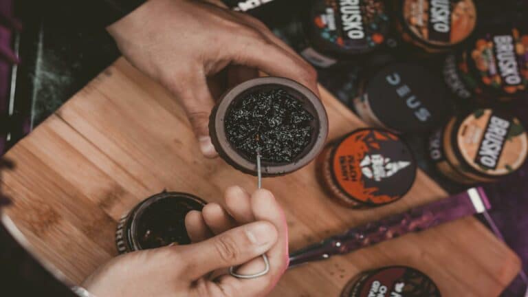 Hands preparing a hookah bowl with tobacco using a tool, surrounded by flavored tobacco containers - Long-tail keyword usage