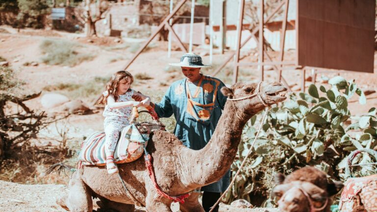 Child enjoying a camel ride guided by a local in traditional attire, surrounded by a desert landscape and cactus plants, highlighting cultural experiences for improved site rankings