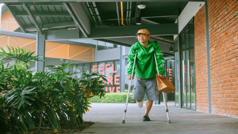 Delivery partner on crutches carrying a package in a modern urban area, showcasing resilience and inclusivity.