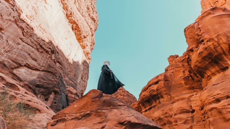 Person in traditional attire exploring red rock canyons under a clear blue sky