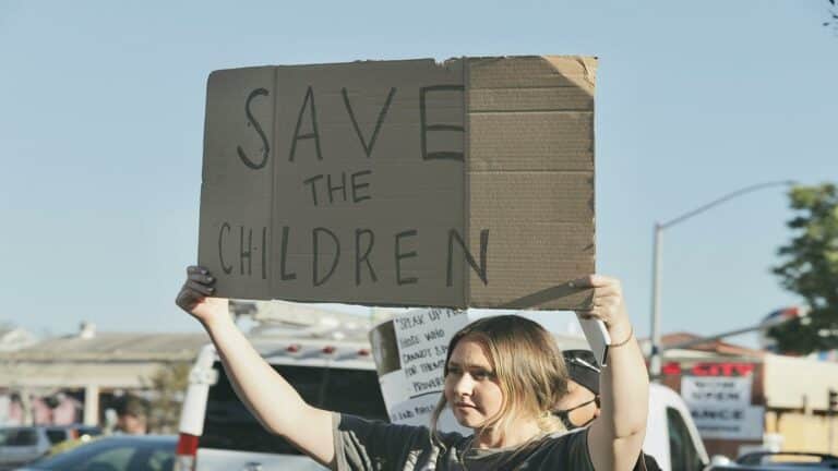 Mobile-friendly design protest sign reading 'Save the Children' held by demonstrator at outdoor rally