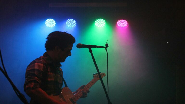 Silhouette of a musician playing guitar under colorful stage lights during a live music performance