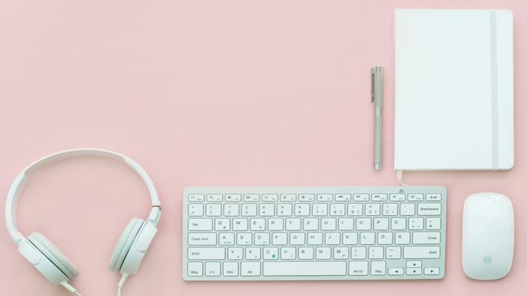 Web Design London workspace essentials featuring headphones, keyboard, mouse, and notebook on a pink background