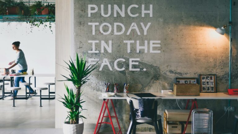 Creative workspace featuring a motivational quote 'Punch Today in the Face' on a concrete wall, with plants and office furniture.