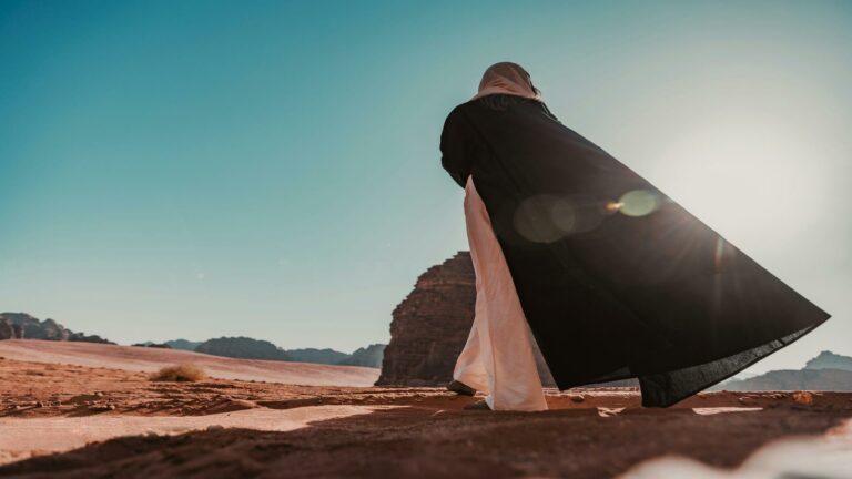 Woman in black abaya walking in a desert landscape under the bright sun