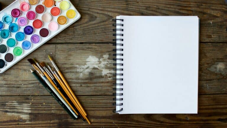 Watercolor paints, brushes, and a blank sketchpad on a wooden table - tools for content marketing creativity