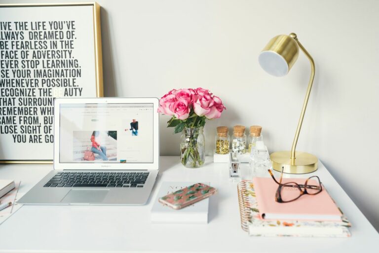 Professional design business workspace with laptop, pink roses, gold desk lamp, notebooks and inspirational quote frame on a clean white desk